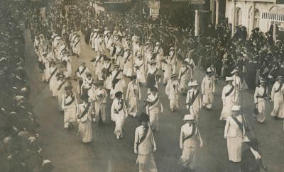 一些妇女在街上游行的黑白照片, 在人群的注视下，她穿着相配的白色套装，系着深色腰带